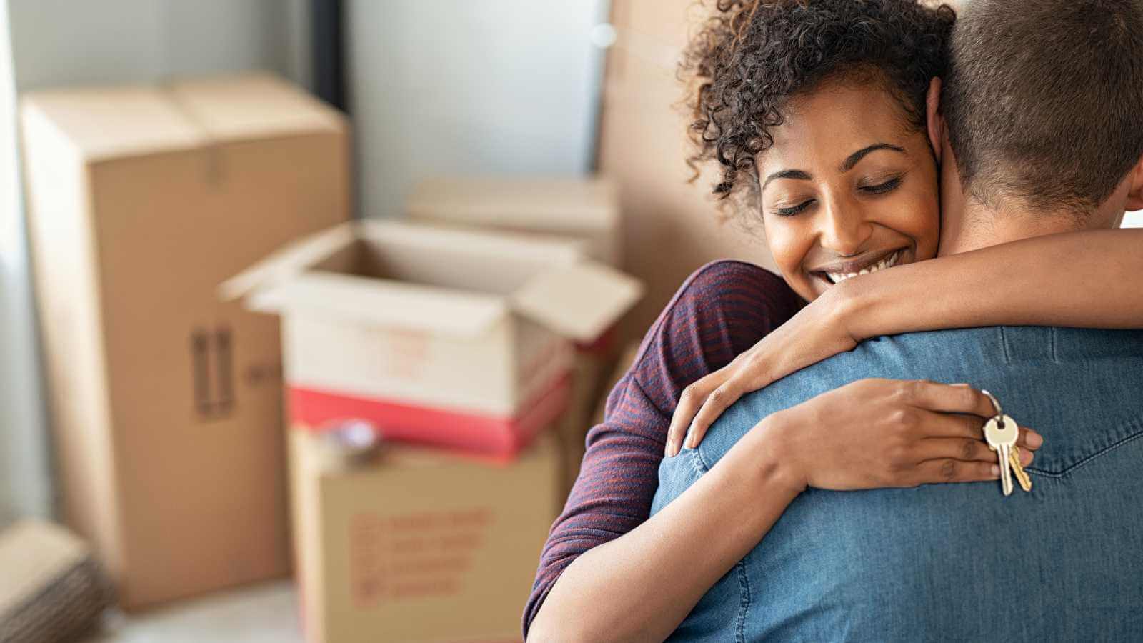 Woman and man hugging with keys and moving boxes